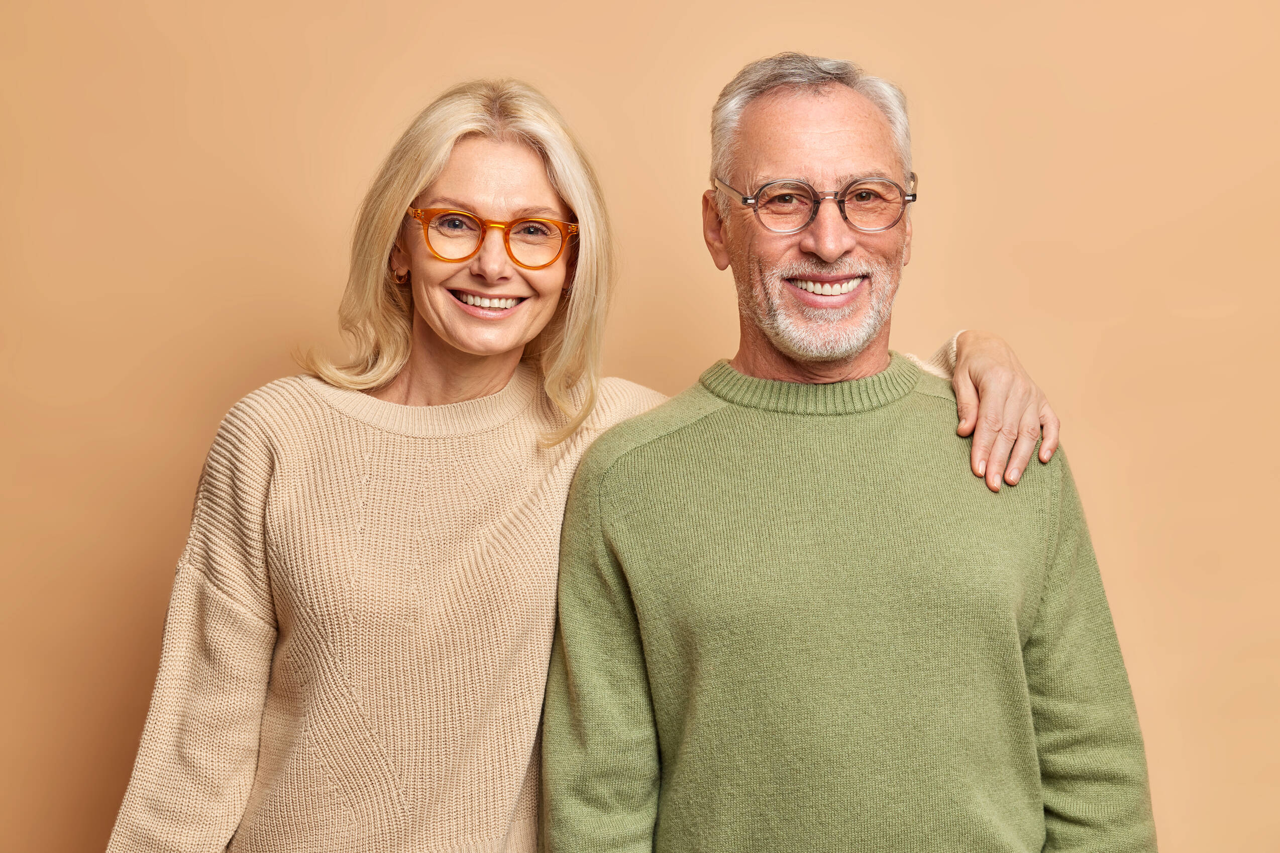 Smiling mature couple embrace look gladfully camera pose family portrait happy children came visit them wear transparent glasses casual jumpers isolated brown wall